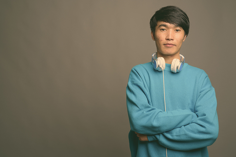 Studio shot of young Asian man wearing headphones against gray background
